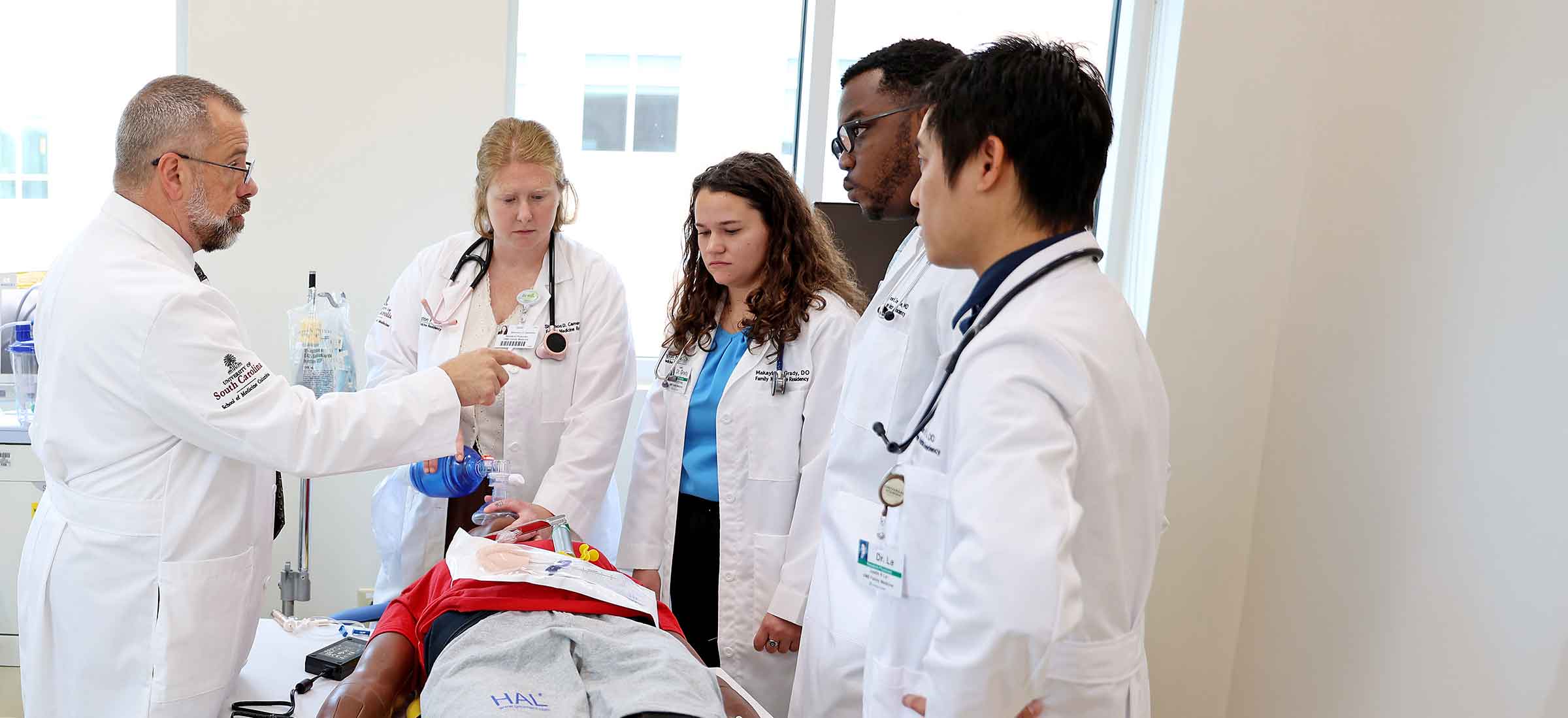 A group of residents practice a procedure with guidance from a doctor.