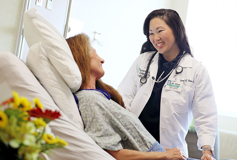 A doctor smiles at a patient resting in a hospital bed.