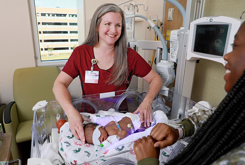A nurse smiles at a mother and her newborn baby.