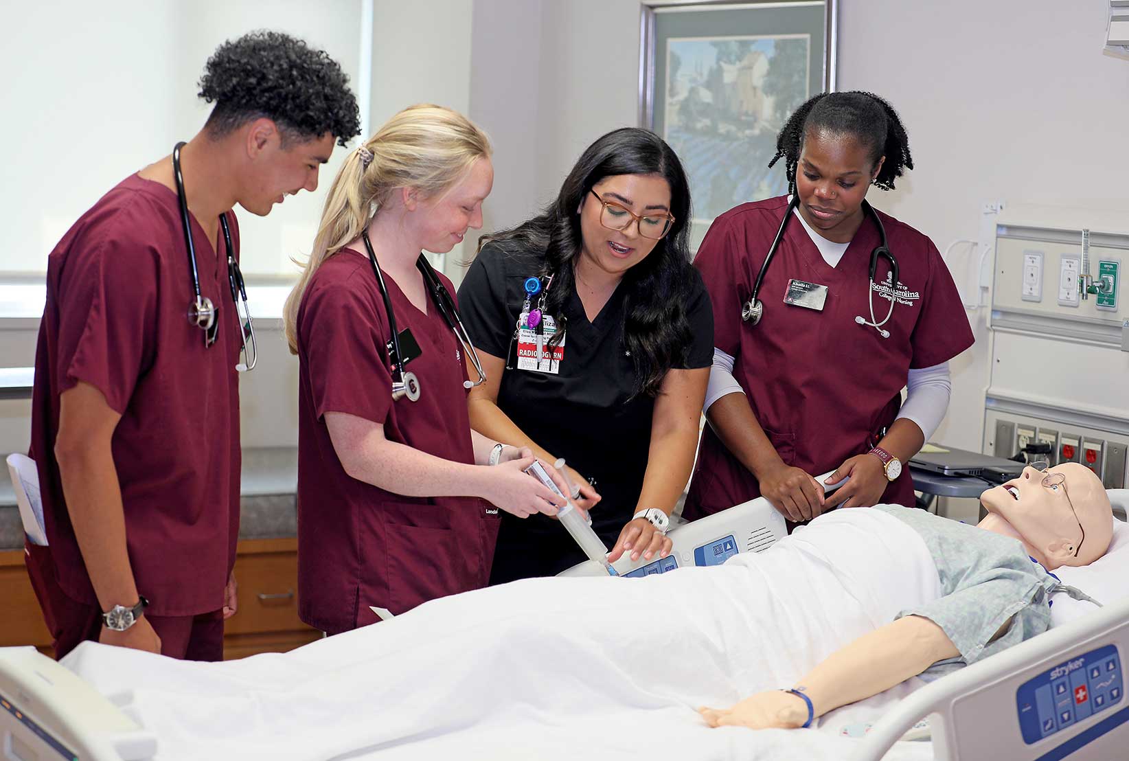 A group of nurse residents practice a procedure on a dummy patient.