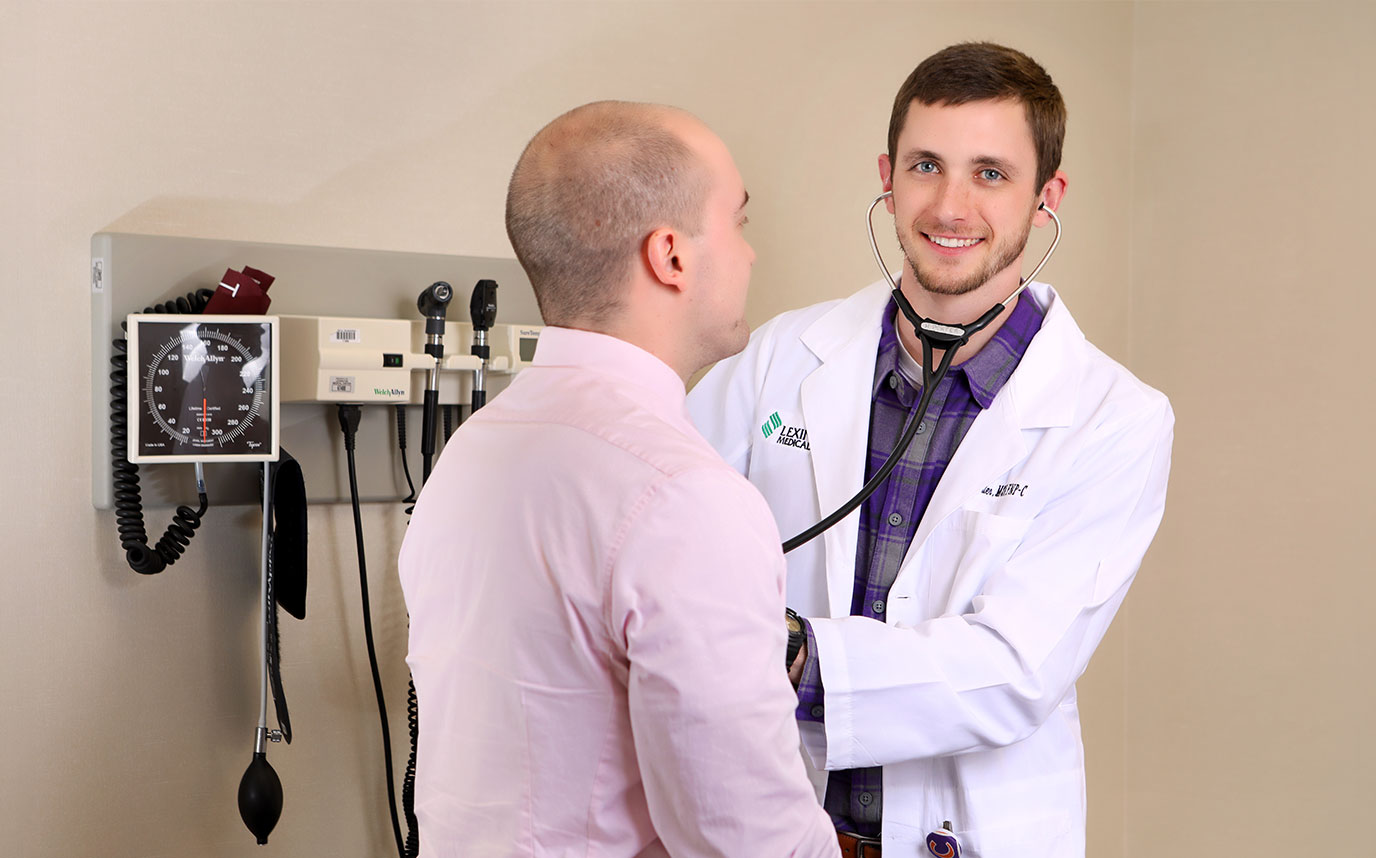 A resident smiles while he listens to a patient's heartbeat.