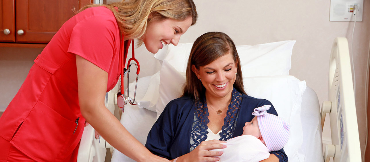 A nurse and mother smiling at a newborn baby.