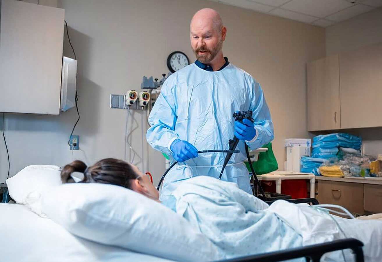 A male doctor holding equipment and speaking to a patient resting in a hospital bed. 