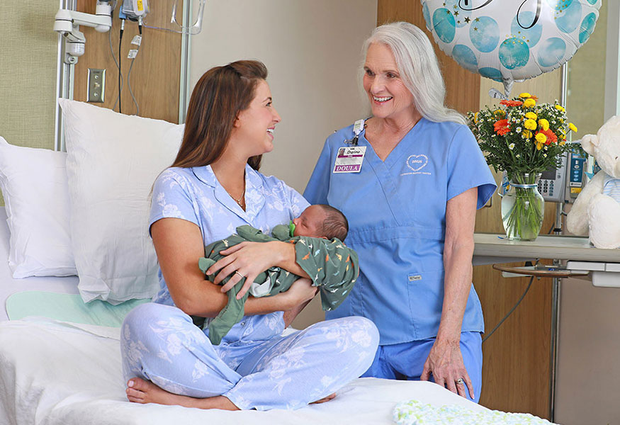 A smiling nurse and mother looking at each other joyfully while the mother holds a newborn baby.