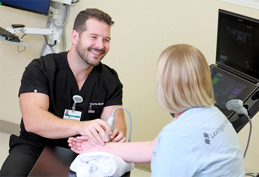 A smiling orthopedist performing an ultrasound on a patient's wrist.