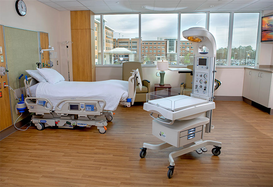 A spacious delivery suite with a hospital bed and bassinet for a baby. 